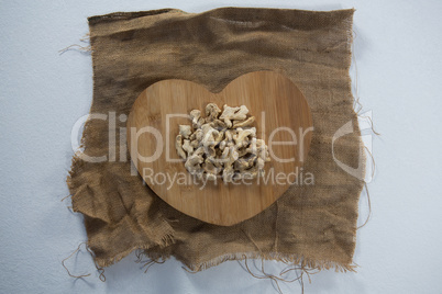 Directly above view of dried gingers on heart shape wooden serving board over burlap