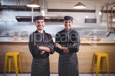 Portrait of smiling young wait staff in standing with arms crossed at coffee shop