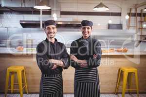 Portrait of smiling young wait staff in standing with arms crossed at coffee shop