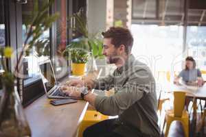 Side view of smiling young man typing on laptop at coffee shop