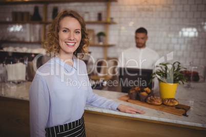 Portrait of confident waitress standing by counter