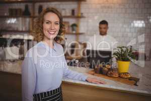 Portrait of confident waitress standing by counter