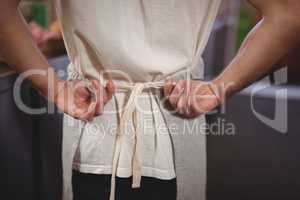Midsection of waiter tying apron at coffee shop
