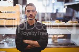 Portrait of confident young waiter standing against counter