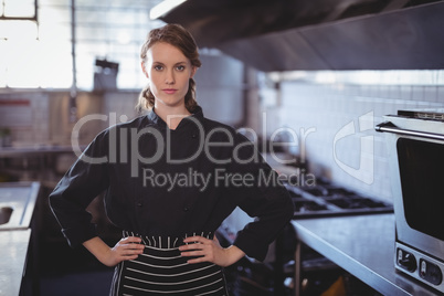 Portrait of young female barista standing with hands on hip in kitchen