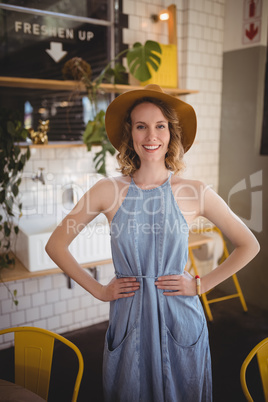 Portrait of smiling woman standing with hands on hip at coffee shop