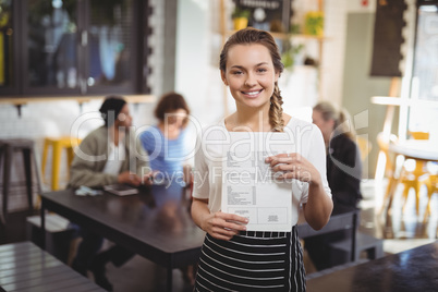 Smiling waitress standing with menu card at cafe