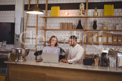 Young male owner and waitress using laptop while sitting at counter