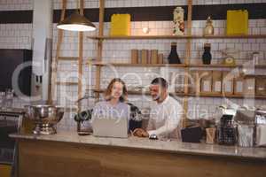 Young male owner and waitress using laptop while sitting at counter