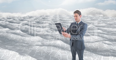 Businessman holding tablet in sea of documents under sky clouds