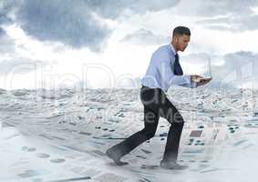 Businessman on laptop in sea of documents under sky clouds