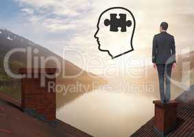 Head with puzzle piece icon and Businessman standing on Roofs with chimney and lake mountain landsca