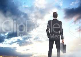 Businessman holding briefcase in cloud opening sky