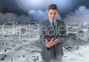 Businessman on tablet in sea of documents under sky clouds