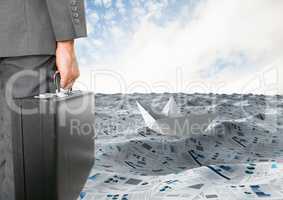 Businessman holding briefcase in sea of documents with paper boat