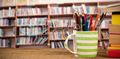 Composite image of stack of books by mug with colored pencils on wooden table