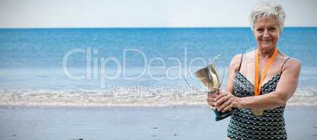 Composite image of portrait of smiling woman in swimwear holding trophy