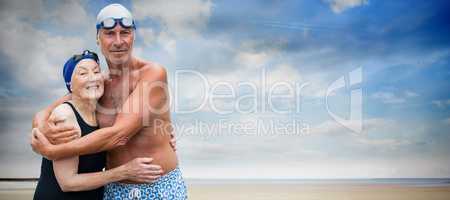 Composite image of smiling senior couple in swimwear embracing while standing