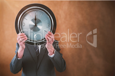 Composite image of businessman holding clock in front of his face