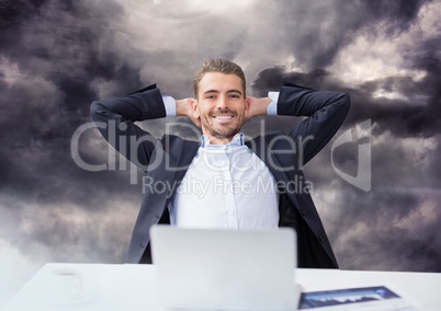 Businessman on laptop under dark sky clouds