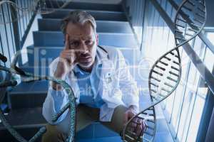 Worried doctor man sitting with 3D DNA strands