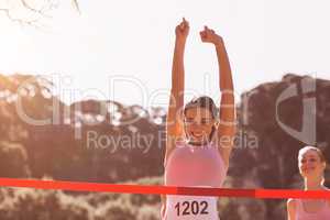 Happy female athlete with arms raised crossing finish line