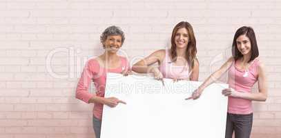 Composite image of women in pink outfits holding board for breast cancer awareness