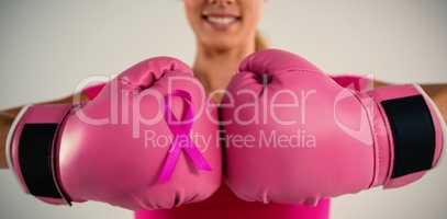 Mid section of smiling woman with boxing gloves and pink ribbon