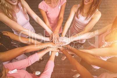 Composite image of women in pink outfits joining in a circle for breast cancer awareness