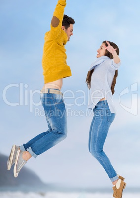 Millennial couple jumping against blurry sky and coastline