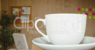White coffee cup on saucer against blurry office with dark overlay