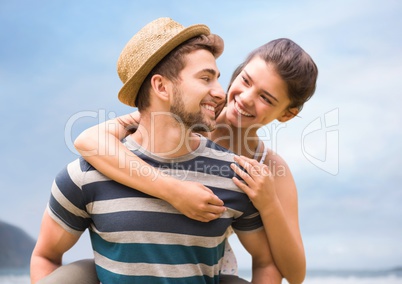Millennial couple embracing against blurry sky and coastline