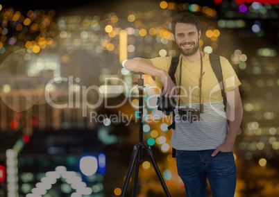 happy photographer rest on tripod in front of the city at night ( with blurred lights) and bokeh ove