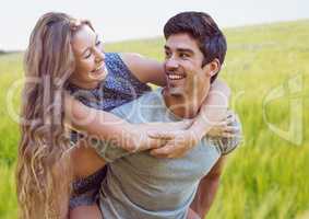 Couple piggy back against blurry meadow