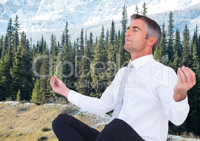 Business man meditating against trees and snowy mountains