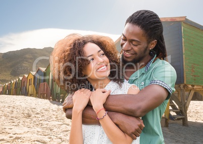Millennial couple embracing against beach huts