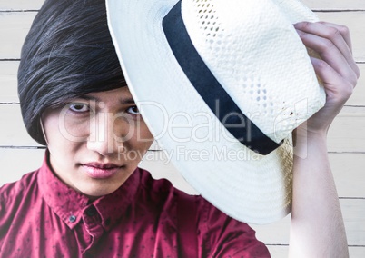 Close up of millennial man tipping hat against white wood panel