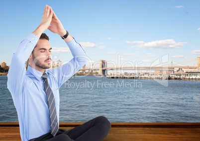 Business man meditating against water and skyline