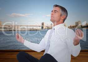 Business man meditating against water and skyline