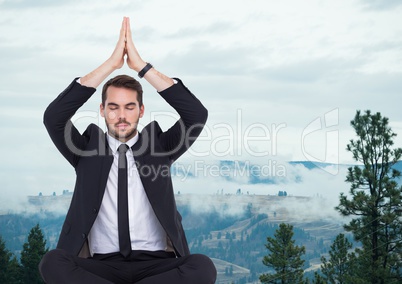 Business man meditating against foggy hills