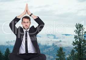 Business man meditating against foggy hills
