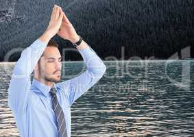 Business man meditating against water and trees on hill