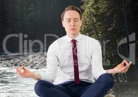 Business man meditating against river