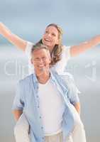 Middle aged couple piggy back against blurry beach