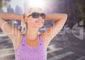 Woman in sunglasses stretching against blurry street with flare