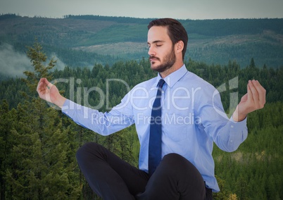 Business man meditating against trees on hills