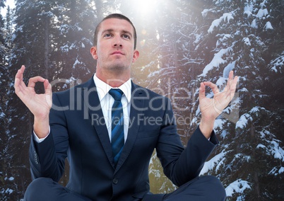 Business man meditating against snowy trees with flare