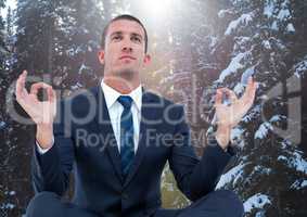 Business man meditating against snowy trees with flare