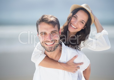 Couple piggy back against blurry beach