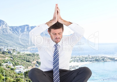 Business man meditating against blurry coastline